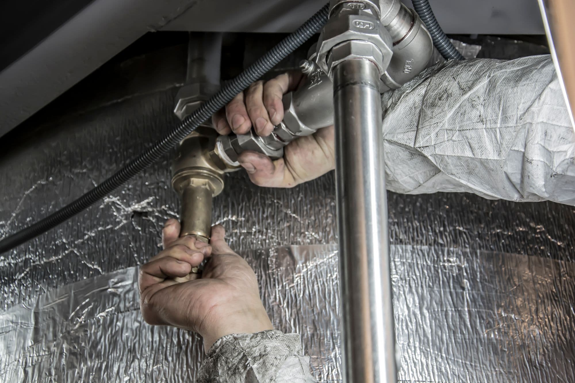 Hands tightening a fitting on a pipe under a sink